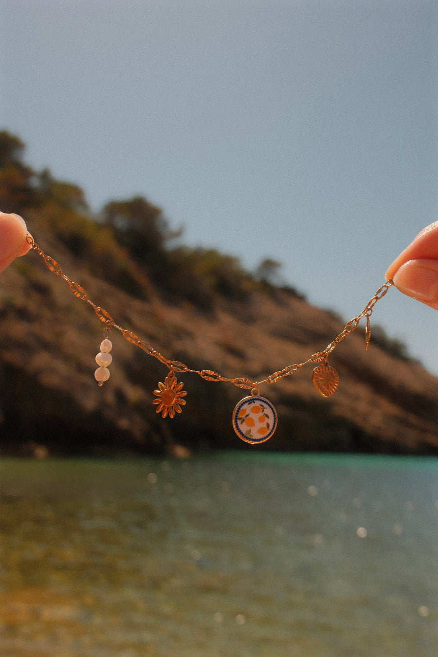 Goudkleurige bedelketting met bloem, medaillons en bedels aan zee